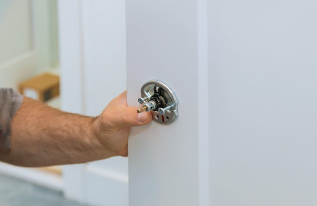 Male carpenter fixing lock in door with home hand close-up.